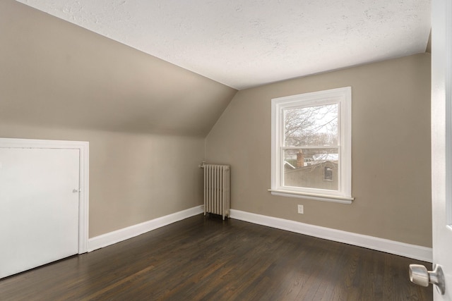 additional living space featuring dark hardwood / wood-style floors, radiator, vaulted ceiling, and a textured ceiling