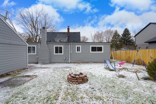 snow covered rear of property with an outdoor fire pit and a playground