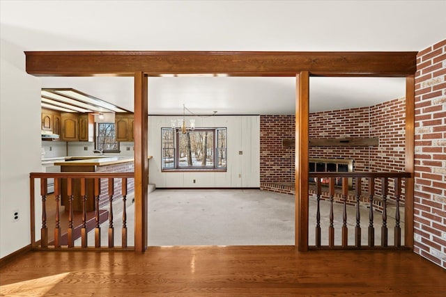 living room featuring sink, an inviting chandelier, beam ceiling, wood-type flooring, and brick wall