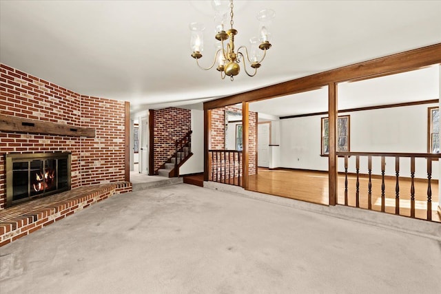 unfurnished living room with an inviting chandelier, a brick fireplace, brick wall, and carpet