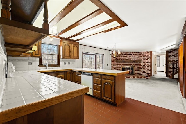 kitchen featuring pendant lighting, a fireplace, tile countertops, stainless steel dishwasher, and kitchen peninsula