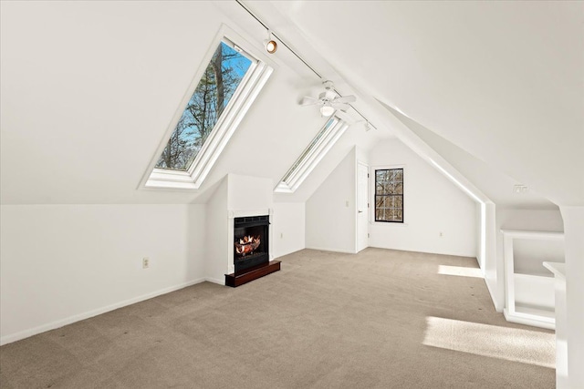 bonus room featuring a multi sided fireplace, lofted ceiling with skylight, light colored carpet, and ceiling fan