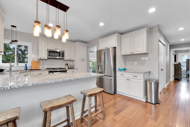 kitchen featuring pendant lighting, sink, white cabinetry, stainless steel appliances, and light stone countertops