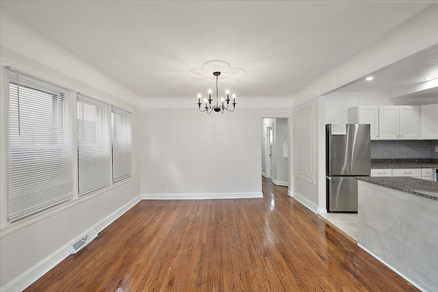 unfurnished dining area featuring an inviting chandelier and hardwood / wood-style floors