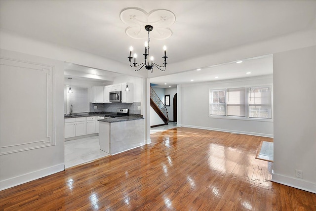 kitchen with appliances with stainless steel finishes, pendant lighting, tasteful backsplash, white cabinetry, and a notable chandelier