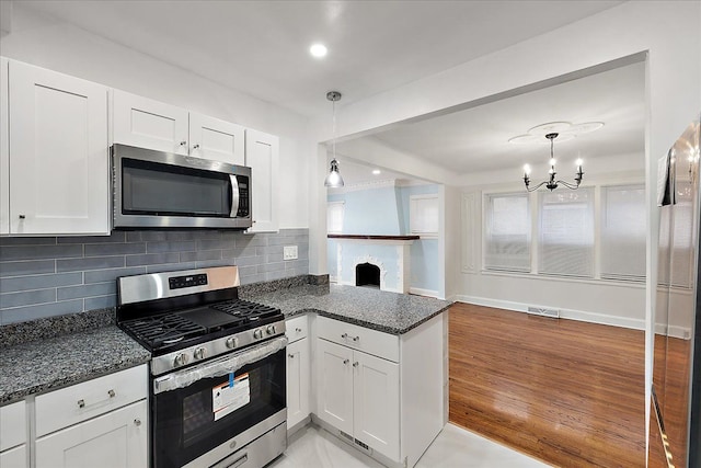 kitchen featuring pendant lighting, white cabinetry, backsplash, stainless steel appliances, and dark stone counters