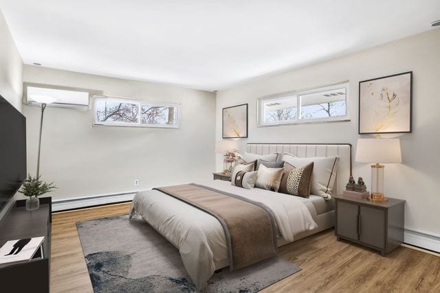 bedroom with baseboard heating, light wood-type flooring, and an AC wall unit