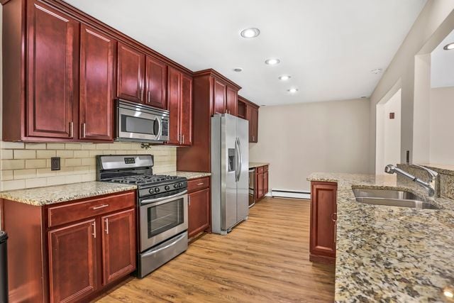 kitchen with sink, a baseboard radiator, stainless steel appliances, and light stone countertops