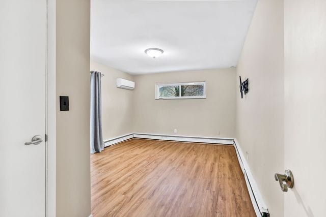 empty room featuring a baseboard heating unit, light hardwood / wood-style flooring, and an AC wall unit