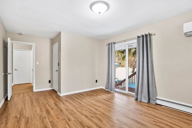 spare room featuring a baseboard radiator, an AC wall unit, and light hardwood / wood-style flooring