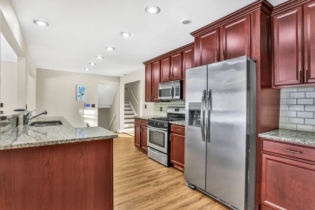 kitchen with sink, decorative backsplash, light stone counters, stainless steel appliances, and light hardwood / wood-style flooring