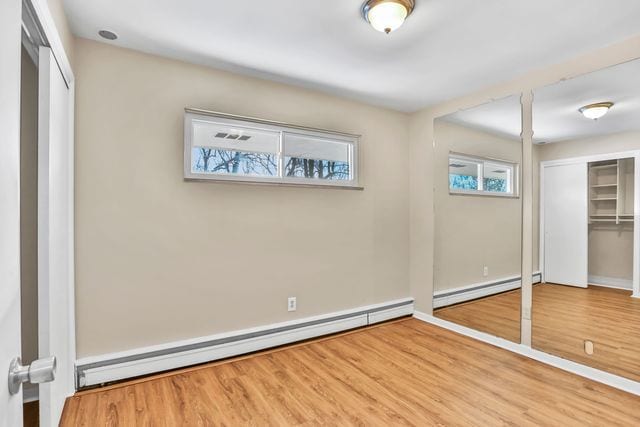 unfurnished bedroom featuring wood-type flooring and baseboard heating