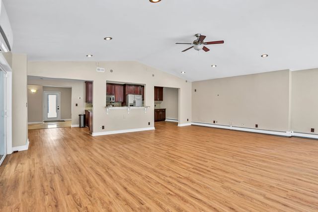 unfurnished living room featuring vaulted ceiling, ceiling fan, light hardwood / wood-style floors, and baseboard heating