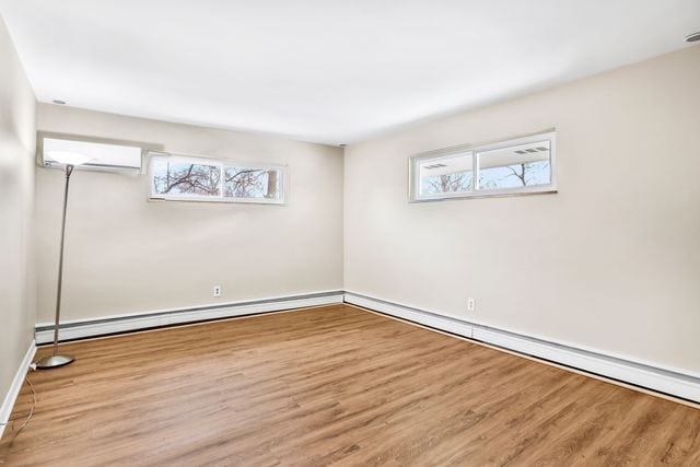 empty room with an AC wall unit, light wood-type flooring, and baseboard heating