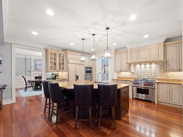 kitchen with cream cabinetry, decorative light fixtures, an island with sink, and premium appliances