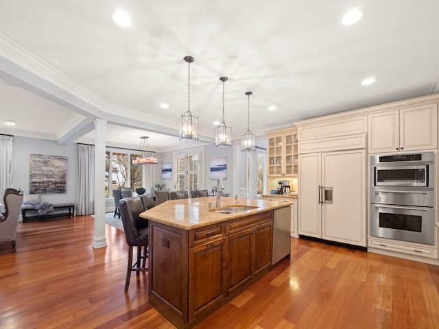 kitchen featuring sink, a kitchen island with sink, stainless steel appliances, decorative light fixtures, and cream cabinetry