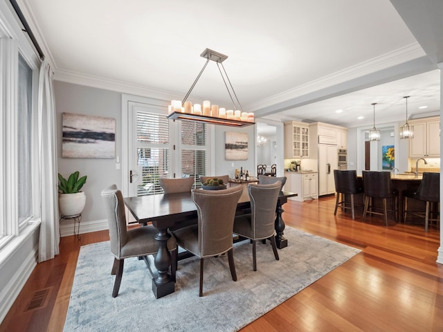 dining area with crown molding, a notable chandelier, and light wood-type flooring