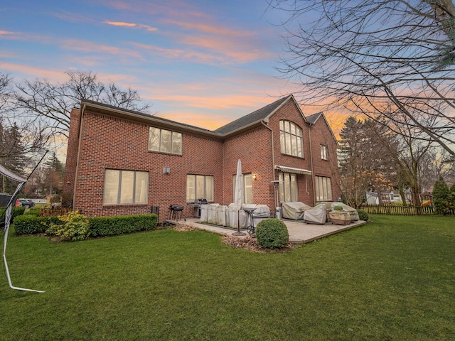 back house at dusk featuring a patio area and a lawn