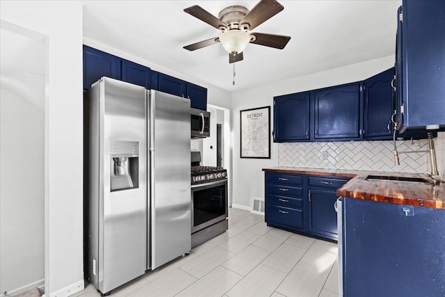 kitchen featuring appliances with stainless steel finishes, sink, backsplash, ceiling fan, and blue cabinetry