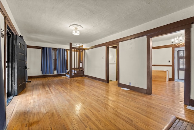 unfurnished room featuring light hardwood / wood-style floors, a textured ceiling, and a notable chandelier