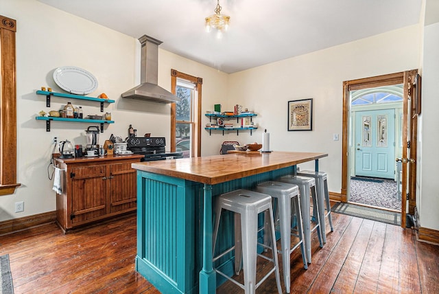 kitchen with a kitchen island, butcher block countertops, black range with electric stovetop, plenty of natural light, and wall chimney exhaust hood