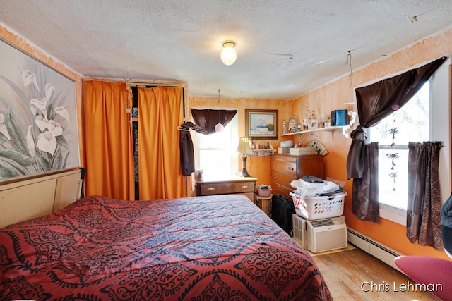 bedroom featuring multiple windows, a baseboard heating unit, a textured ceiling, and light wood-type flooring