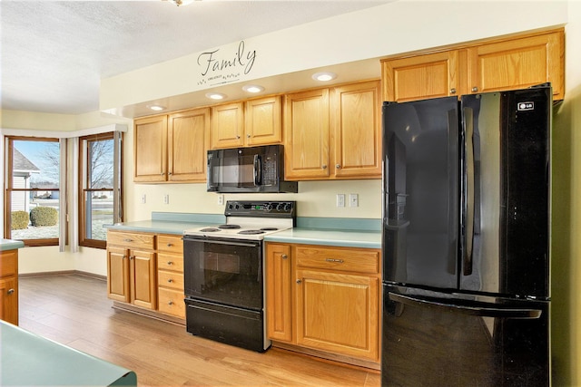 kitchen with black appliances, a textured ceiling, and light wood-type flooring