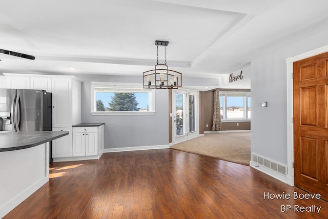 interior space featuring stainless steel refrigerator with ice dispenser, decorative light fixtures, dark hardwood / wood-style floors, a raised ceiling, and white cabinets