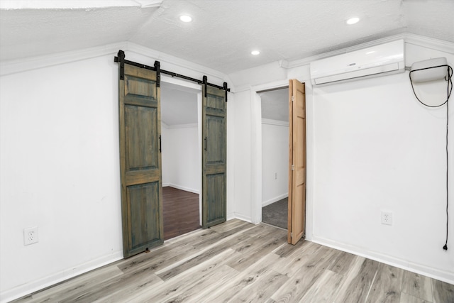 unfurnished bedroom with an AC wall unit, lofted ceiling, light wood-type flooring, a barn door, and a textured ceiling