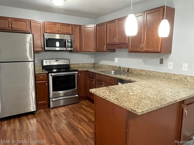 kitchen featuring sink, dark wood-type flooring, appliances with stainless steel finishes, hanging light fixtures, and kitchen peninsula