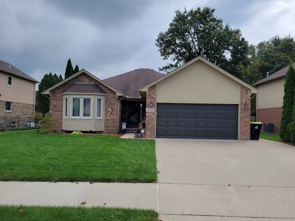 ranch-style house featuring a garage, a front lawn, and central air condition unit