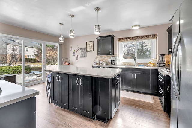 kitchen featuring a kitchen island, pendant lighting, stainless steel refrigerator, sink, and light wood-type flooring