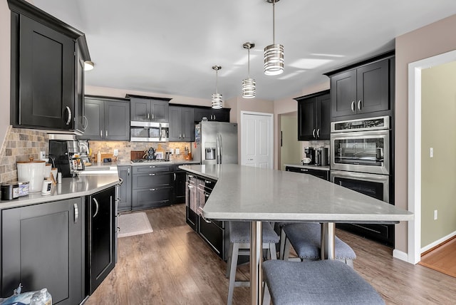 kitchen with dark wood-type flooring, a kitchen island, pendant lighting, stainless steel appliances, and decorative backsplash