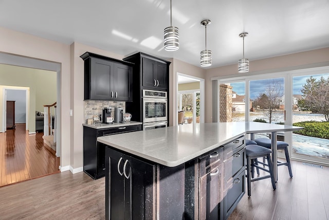 kitchen with a kitchen island, double oven, tasteful backsplash, hanging light fixtures, and hardwood / wood-style flooring