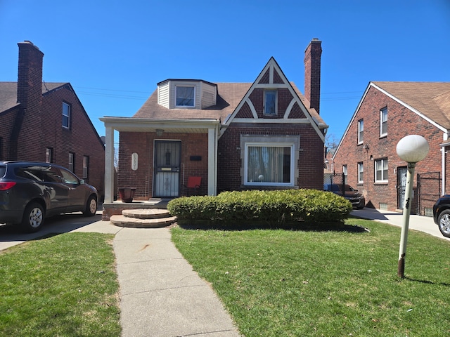tudor house featuring a chimney, a porch, a front lawn, and brick siding