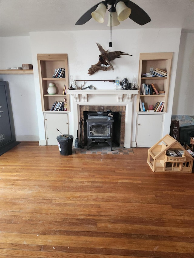 living room featuring a wood stove, hardwood / wood-style floors, ceiling fan, and built in shelves