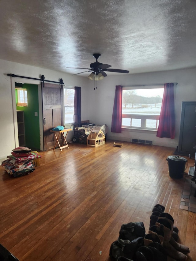 living room featuring wood-type flooring, a barn door, ceiling fan, and a textured ceiling