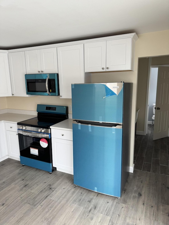 kitchen featuring fridge, white cabinets, light wood-type flooring, and stainless steel range with electric stovetop