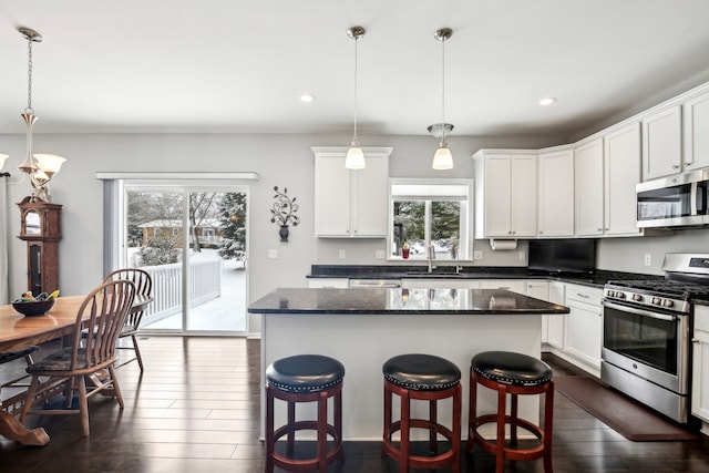 kitchen with decorative light fixtures, a kitchen island, white cabinets, and appliances with stainless steel finishes