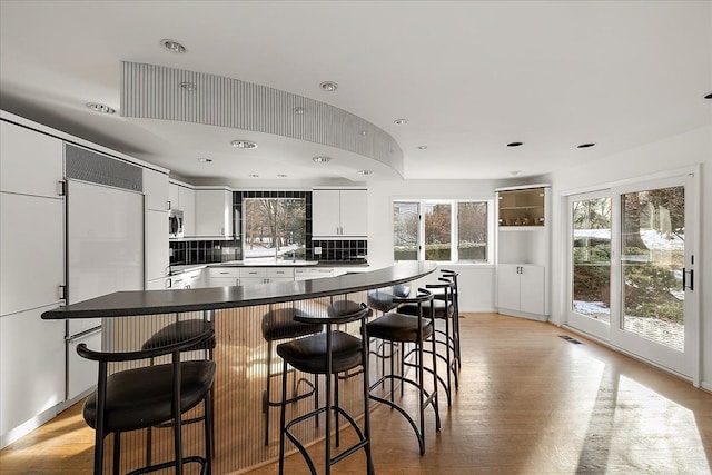 kitchen featuring a kitchen breakfast bar, white cabinets, light wood-type flooring, and decorative backsplash