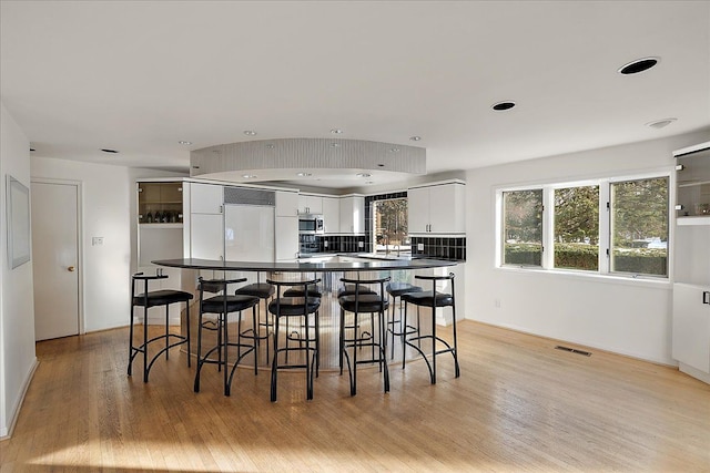 kitchen with light wood-type flooring, a breakfast bar, paneled fridge, and white cabinets