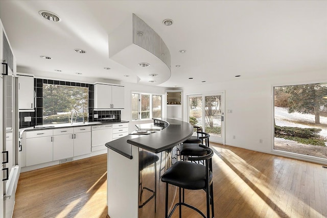 kitchen featuring sink, a kitchen breakfast bar, tasteful backsplash, light hardwood / wood-style floors, and white cabinets