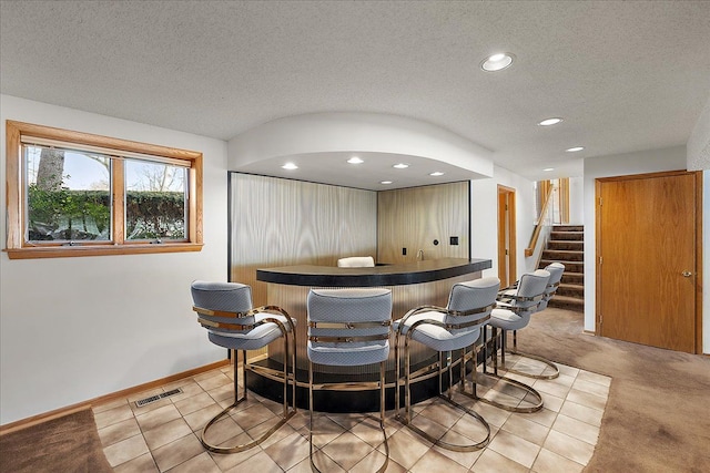 bar featuring light colored carpet and a textured ceiling