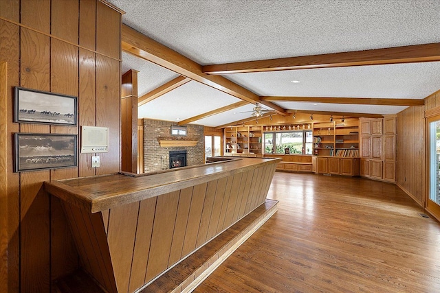 kitchen with wooden walls, wood-type flooring, kitchen peninsula, a brick fireplace, and a textured ceiling