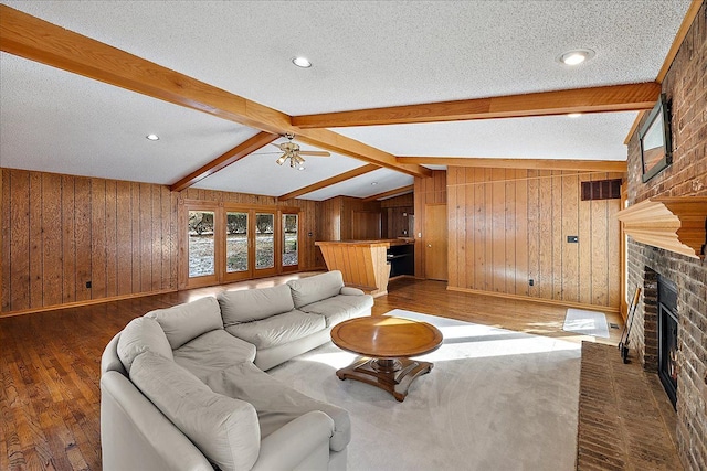 living room with a fireplace, vaulted ceiling with beams, dark hardwood / wood-style flooring, ceiling fan, and a textured ceiling