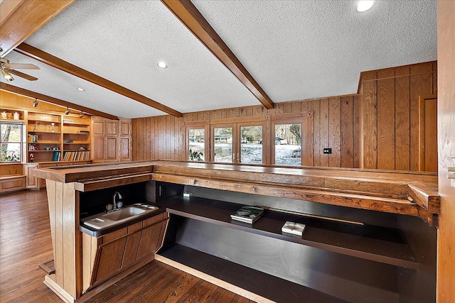 kitchen featuring ceiling fan, wooden walls, dark hardwood / wood-style floors, lofted ceiling with beams, and a textured ceiling