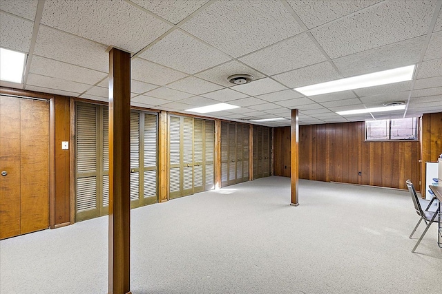 basement with a paneled ceiling, carpet floors, and wood walls