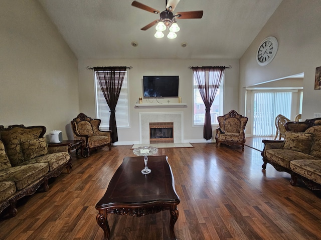 living room with ceiling fan, dark hardwood / wood-style flooring, a tiled fireplace, and high vaulted ceiling