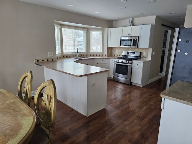 kitchen featuring appliances with stainless steel finishes, sink, white cabinets, decorative backsplash, and kitchen peninsula