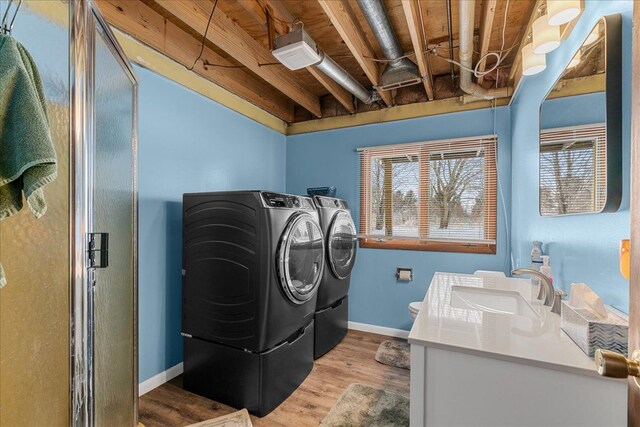 laundry room featuring sink, washing machine and clothes dryer, and light hardwood / wood-style flooring